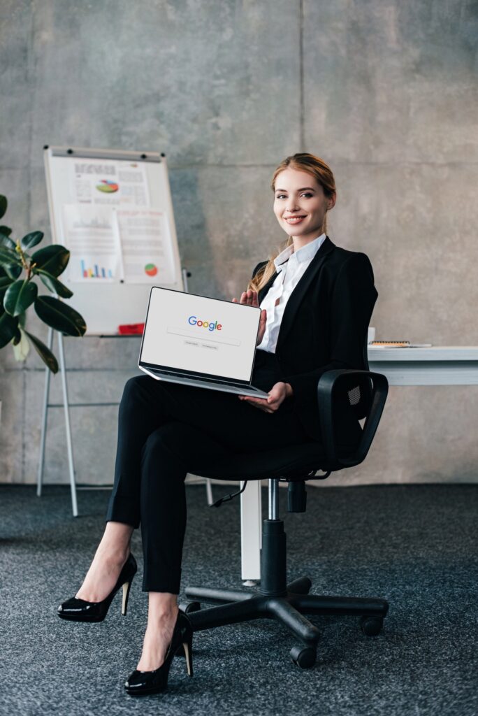 pretty smiling businesswoman sitting in chair and holding laptop with google on display